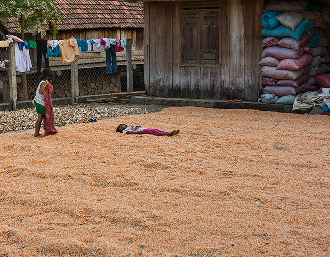 Children play in the corn that is out in the sun to dry